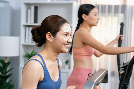 Energetic and strong athletic asian woman running on elliptical running machine at home with workout...