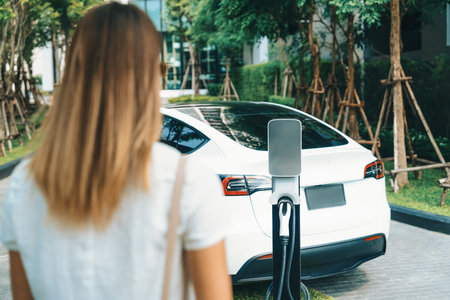 Young woman travel with EV electric car charging in green sustainable city outdoor garden in summer. Urban sustainability lifestyle by green clean rechargeable energy of electric BEV vehicle innardsの写真素材