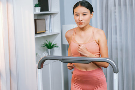 Energetic and strong athletic asian woman running running machine at home. Pursuit of fit physique...