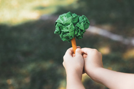 Little boy holding recycled paper tree to promote eco lifestyle on reducing, reusing, and natural...