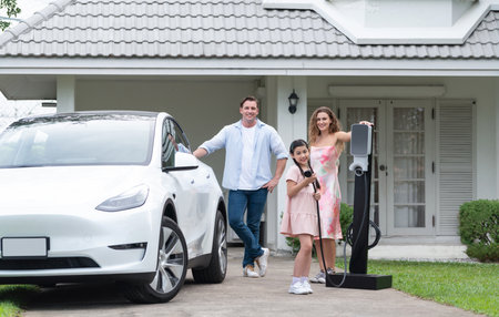 Modern family with environmental conscious recharging EV car with home EV charging station, Happy family with little young girl holding and pointing EV charger at camera. Synchronosの写真素材