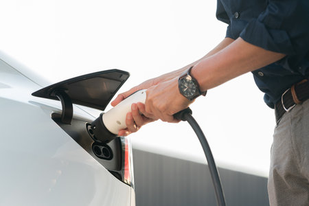 Young man put EV charger to recharge electric cars battery from charging station in city commercial...