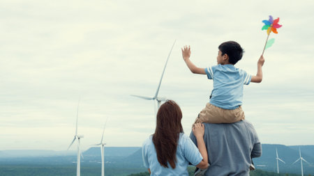 Concept of progressive happy family enjoying their time at the wind turbine farm. Electric generator from wind by wind turbine generator on the country side with hill and mountain on the horizon.の写真素材