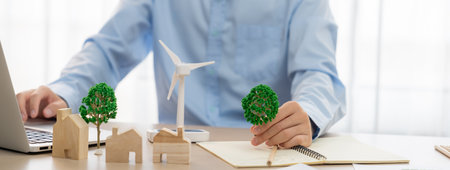 Professional architect plans to use green design in an eco house. Skilled engineer design an eco house blueprint by using laptop on table with house and windmill model scatter around. Delineation.の写真素材