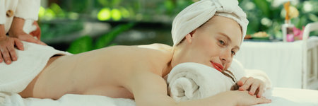 Beautiful young woman lies on white spa bed during having back massage. Attractive caucasian woman having back massage surrounded by natural environment. Relaxing and healthy concept Tranquility.の写真素材