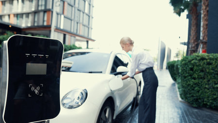Progressive businesswoman install charger plug from charging station to his electric car before driving around city center. Eco friendly rechargeable car powered by sustainable and clean energy.の写真素材