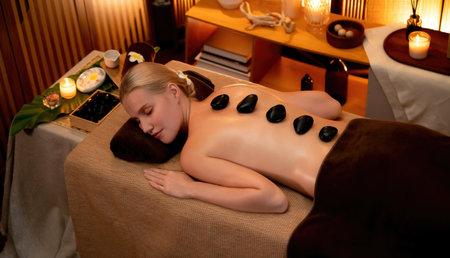 Hot stone massage at spa salon in luxury resort with warm candle light, blissful woman customer enjoying spa basalt stone massage glide over body with soothing warmth. Quiescentの写真素材