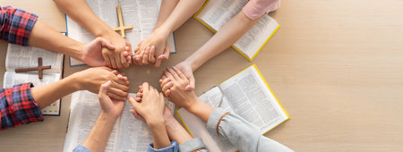 Cropped image of group of people praying together while holding hand on holy bible book at wooden...