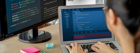 Cropped image of female web developer coding on laptop while computer displayed program and software...
