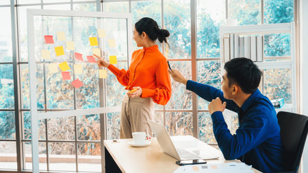 Business people work on project planning board in office and having conversation with coworker...