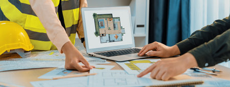 Professional architect shows mistake structure in blueprint while analysis and comparison with picture in laptop on table with blueprint and architectural equipment. Cropped image. Delineation.の写真素材