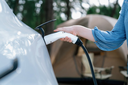 Holiday camping vacation traveling to nature countryside with electric car, woman recharge EV car...