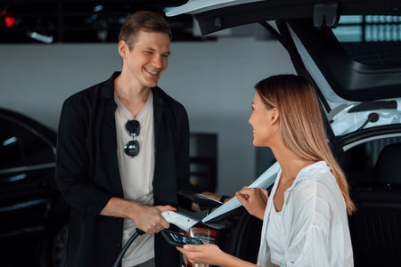 Young couple travel with EV electric car to shopping center parking lot charging in downtown city showing urban sustainability lifestyle by green clean rechargeable energy of electric vehicle innardsの写真素材