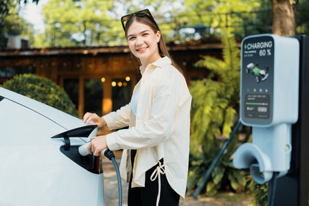 Young woman and sustainable urban commute with EV electric car recharging at outdoor cafe in springtime garden, green city sustainability and environmental friendly EV car. Expedientの写真素材