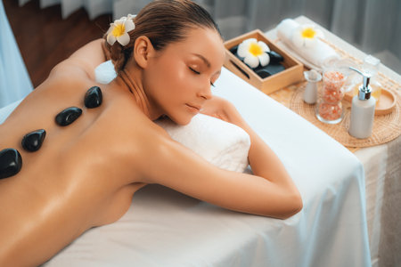 Hot stone massage at spa salon in luxury resort with day light serenity ambient, blissful woman customer enjoying spa basalt stone massage glide over body with soothing warmth. Quiescentの写真素材