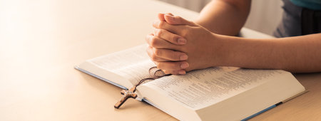 Asian male folded hand prayed on holy bible book while holding up a pendant crucifix. Spiritual,...