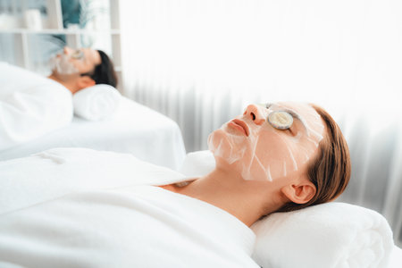 Serene daylight ambiance of spa salon, couple customer indulges in rejuvenating with luxurious cucumber facial mask. Facial skincare treatment and beauty care concept. Quiescentの写真素材