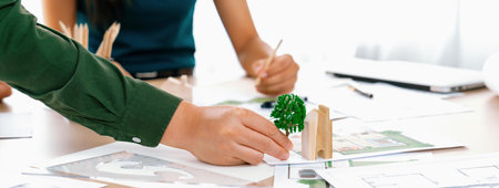 Professional architect team discuss about green design of eco house on meeting table with blueprint...