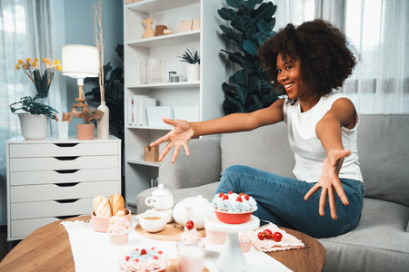 Beautiful young African blogger presenting piece of cupcake in concept showing special cuisine in pastel color. Content creating of social media with favorite sweets bakery dish. Tastemaker.の写真素材