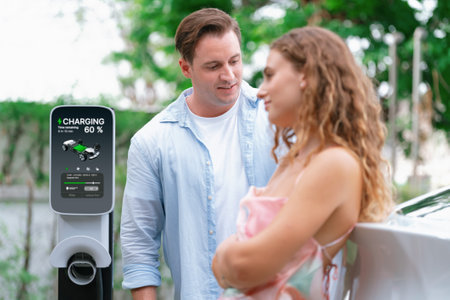 Happy and lovely couple with eco-friendly conscious recharging electric vehicle from EV charging station. EV car technology utilized as alternative transportation for future sustainability. Synchronosの写真素材