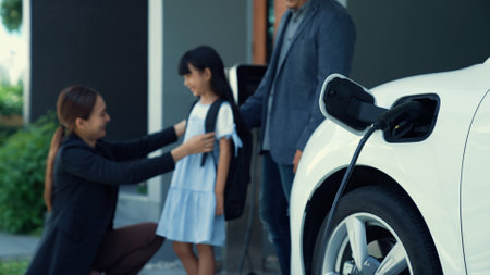 Progressive parents with electric vehicle and home charging station. Happy family with daughter giving each other high fives before leave for school. Alternative future transportation concept of EVsの写真素材