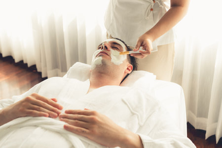 Serene ambiance of spa salon, man customer indulges in rejuvenating with luxurious face cream massage with modern daylight. Facial skin treatment and beauty care concept. Quiescentの写真素材