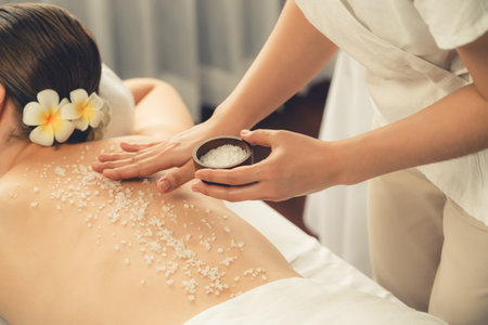 Woman customer having exfoliation treatment in luxury spa salon with warmth candle light ambient. Salt scrub beauty treatment in health spa body scrub. Quiescentの写真素材