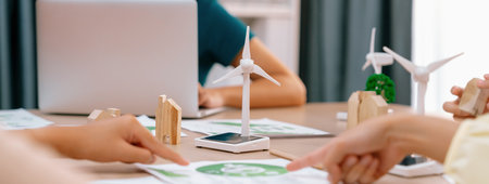 Windmill model represented using renewable energy placed during presenting green business on table with wooden block and environmental document scatter around. Closeup. Delineation.の写真素材