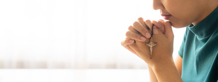 Praying female hand holding cross while praying to god faithfully. Concept of hope, religion, faith, christianity and god blessing for happiness. Bright light, white blurring background. Burgeoning.の写真素材