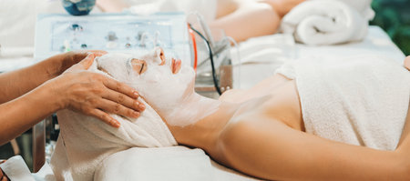Beautiful young women lie on spa bed while having facial massage from professional doctor. Attractive female with beautiful skin surrounded by electric facial machine. Tranquility.の写真素材