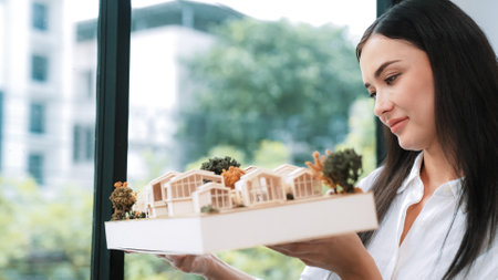 Close up of skilled young beautiful caucasian architect lift house model left side and right sight to check and focus on inspecting mistake point at modern office with blueprint. Immaculate.の写真素材