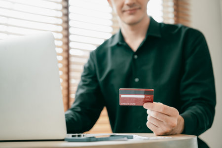Young man using laptop with credit card for internet banking, online shopping E commerce by online payment gateway at home office. Modern and convenience online purchasing with debit card. Unveilingの写真素材