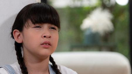 Sad little girl sitting alone in living room crying, feeling lonely. Young girl experiencing social isolation punishment or neglect from parent led to anxiety childhood. Panorama Synchronosの写真素材