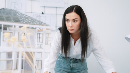 Young beautiful caucasian architect puts blueprint on the table and compare with house model while inspect hos model construction carefully at modern office with blueprint striped behind. Immaculate.の写真素材