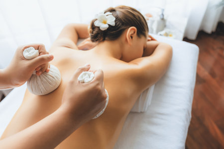 Hot herbal ball spa massage body treatment, masseur gently compresses herb bag on woman body. Tranquil and serenity of aromatherapy recreation in day lighting ambient at spa salon. Quiescentの写真素材
