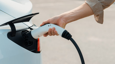 Closeup hand put EV charger to recharge electric cars battery from charging station in city commercial parking lot. Rechargeable EV car for sustainable environmental friendly urban travel. Expedientの写真素材