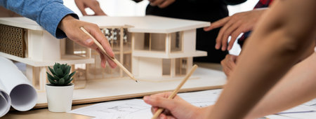 Architect team analysis and brainstorming about house construction at meeting table with house model, blueprint and architectural equipment scatter around. Creative design and teamwork. Burgeoning.の写真素材