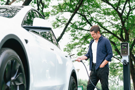 Man recharging battery for electric car during road trip travel EV car in natural forest or national park. Eco friendly travel during vacation and holiday. Exaltの写真素材