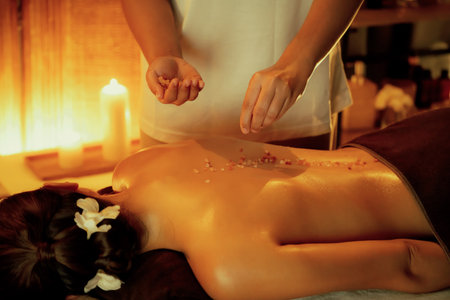 Woman customer having exfoliation treatment in luxury spa salon with warmth candle light ambient. Salt scrub beauty treatment in Health spa body scrub. Quiescentの写真素材