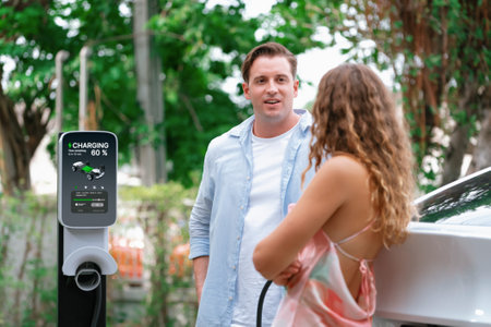 Happy and lovely couple with eco-friendly conscious recharging electric vehicle from EV charging station. EV car technology utilized as alternative transportation for future sustainability. Synchronosの写真素材