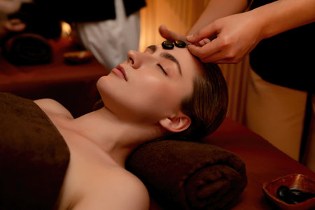 Caucasian couple enjoying relaxing anti-stress head massage with hot stone and pampering facial beauty skin recreation leisure in warm candle light ambient salon spa in resort or hotel. Quiescentの写真素材