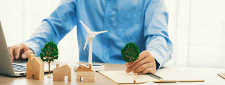 Professional architect plans to use green design in an eco house. Skilled engineer design an eco house blueprint by using laptop on table with house and windmill model scatter around. Delineation.の写真素材
