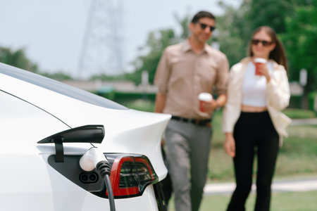Young couple with coffee cup, recharge electric cars battery from EV charging station in green city park. Sustainable and eco friendly EV car with urban and shopping lifestyle. Expedientの写真素材