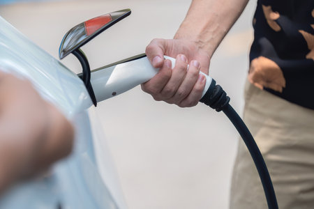 Hand insert EV charger plug into electric vehicle to recharge EV car battery from outdoor charging station. Fresh daylight environment with alternative clean and sustainable energy concept. Perpetualの写真素材