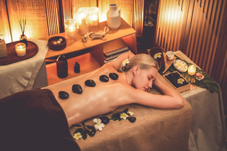 Hot stone massage at spa salon in luxury resort with warm candle light, blissful woman customer enjoying spa basalt stone massage glide over body with soothing warmth. Quiescentの写真素材