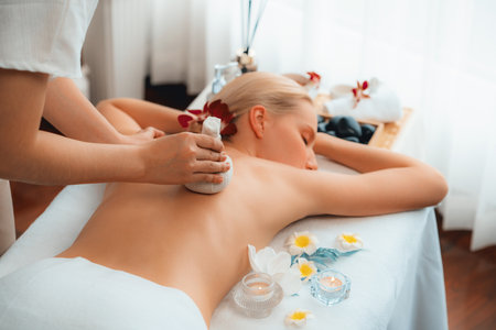 Hot herbal ball spa massage body treatment, masseur gently compresses herb bag on woman body. Tranquil and serenity of aromatherapy recreation in day lighting ambient at spa salon. Quiescentの写真素材