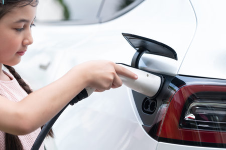 Little young girl learn about eco-friendly and energy sustainability as she recharge electric vehicle from EV charging station. EV car and sustainable future generation concept. Synchronosの写真素材