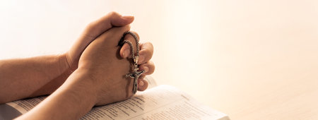 Asian male folded hand prayed on holy bible book while holding up a pendant crucifix. Spiritual,...