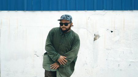 Hipster dancing b-boy foot step at street with blue wall. Asian break dancer practice street dance while stretch arms. Hip hop choreographer perform energetic dance. Outdoor sport 2024. Endeavor.の写真素材