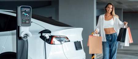 Young woman travel with EV electric car to shopping center parking lot charging in downtown city showing urban sustainability lifestyle by green clean rechargeable energy of electric vehicle innardsの写真素材
